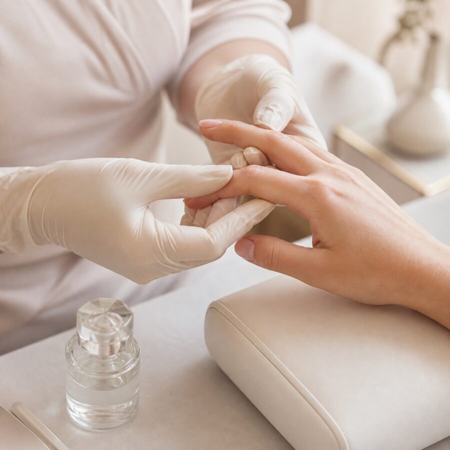 Professional nail technician in gloves gently examining a client hand